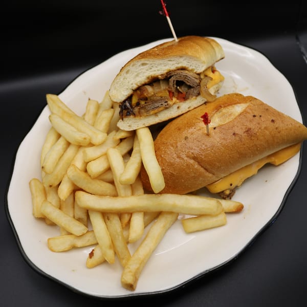 A Johnson Diner & Bar cheesesteak sandwich with fries on a white plate against a dark background.