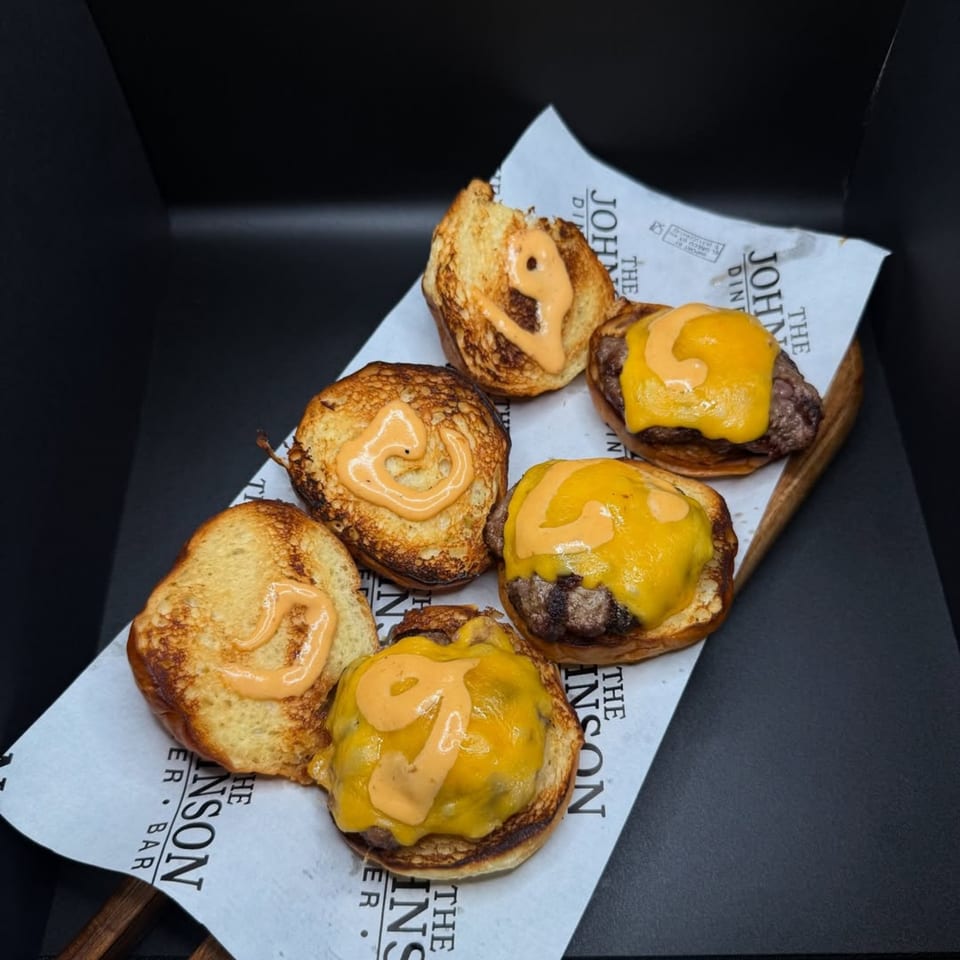 Six mini cheeseburgers with melted cheese and special sauce on toasted buns, served on branded paper.