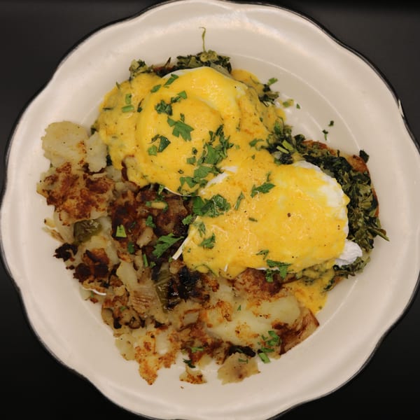 Eggs Benedict with hollandaise sauce, hash browns, and spinach on a white plate.