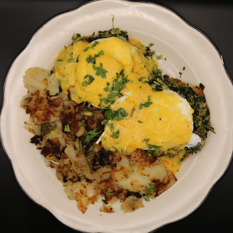 Eggs Benedict with hollandaise sauce, hash browns, and spinach on a white plate.