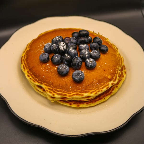 Stack of golden pancakes topped with fresh blueberries and powdered sugar on a white plate.