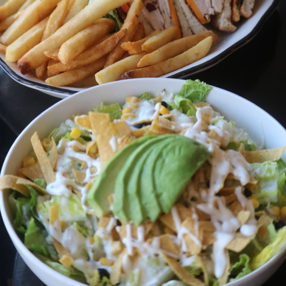A fresh salad with avocado, corn, and tortilla strips, next to a plate of golden fries.
