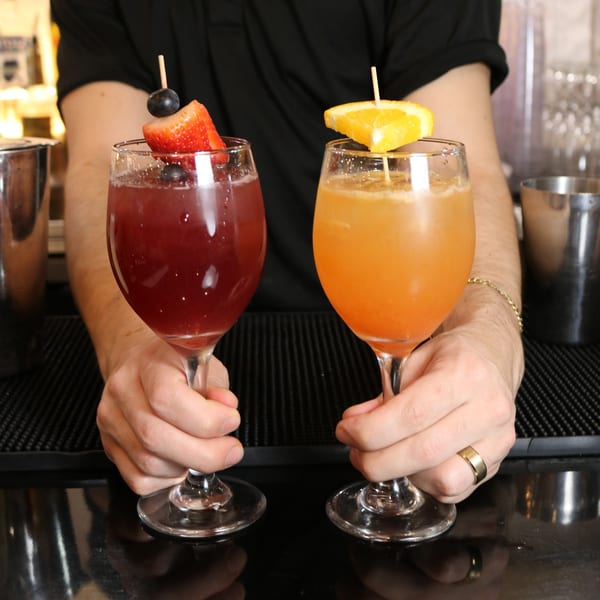 Bartender holding two Johnson Diner & Bar cocktails, one red with berries, one orange with citrus.