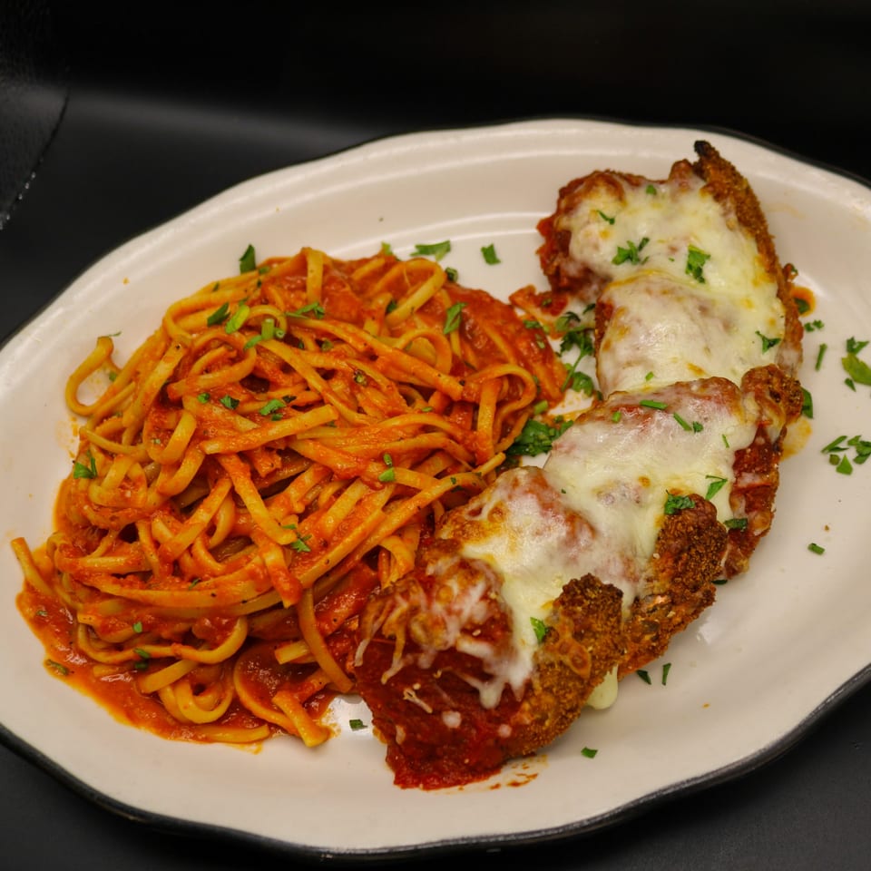 Chicken Parmesan with melted mozzarella cheese and a side of linguine pasta with red sauce.